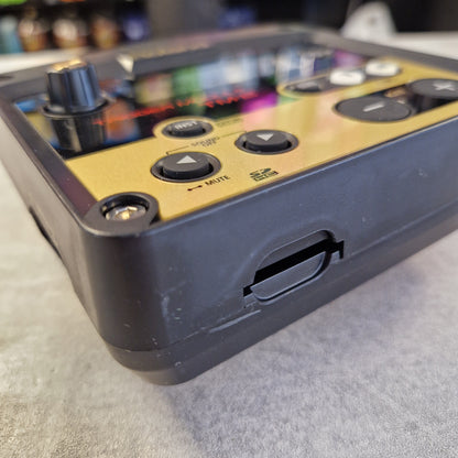 Pre-Owned Roland TM-2 Close-up of a black audio pedal or controller with a gold faceplate, showing buttons, a rotary knob, and a USB-C port on a gray textured surface.