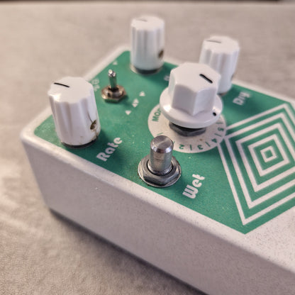 Pre-Owned EarthQuaker Close-up of a guitar effects pedal with a green faceplate, white knobs, and a silver footswitch on a light gray surface.