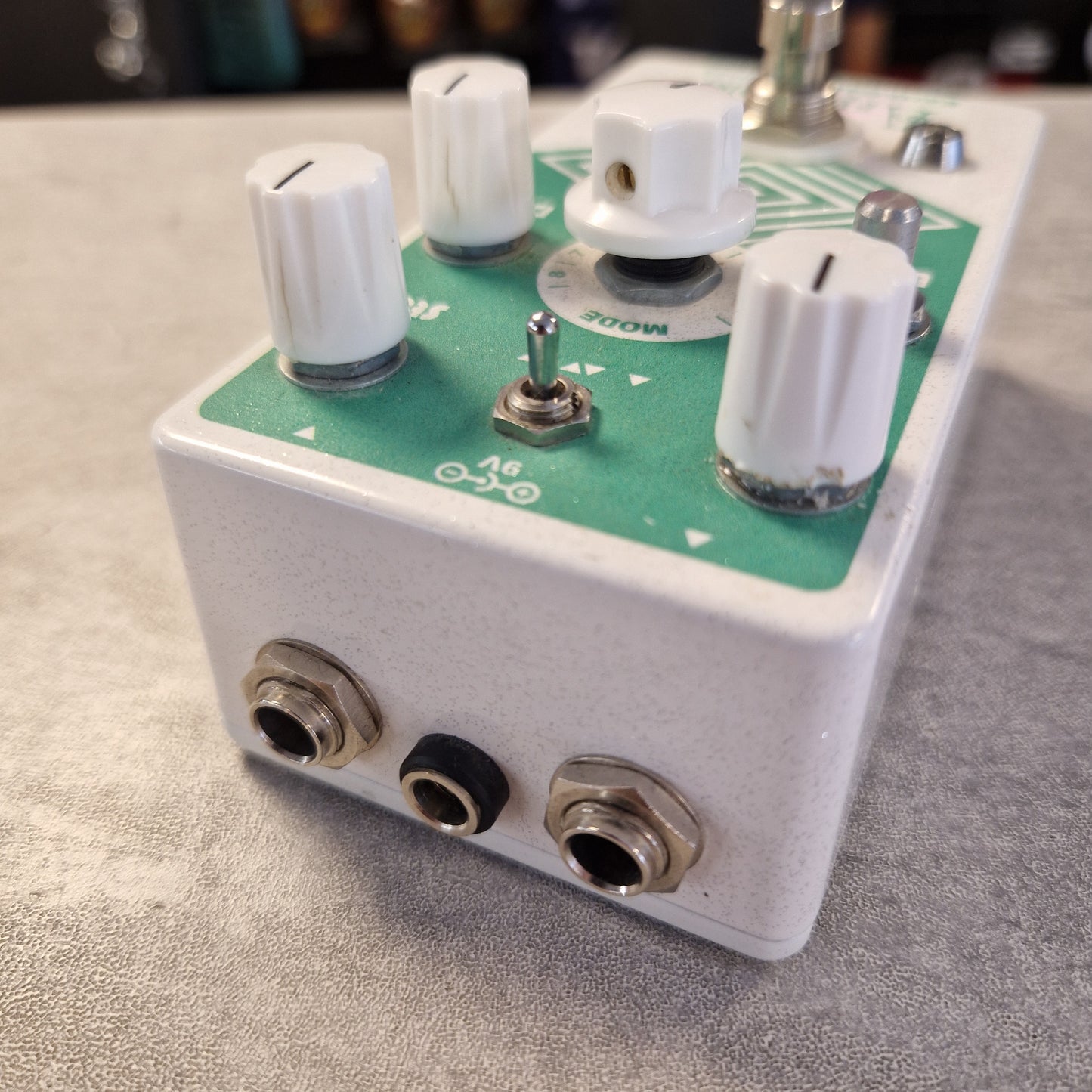 Pre-Owned EarthQuaker A close-up shot of a guitar effects pedal with a white metal casing, a green circuit board, white knobs, and metal input/output jacks, resting on a gray textured surface.