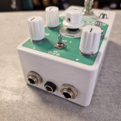 Pre-Owned EarthQuaker A close-up shot of a guitar effects pedal with a white metal casing, a green circuit board, white knobs, and metal input/output jacks, resting on a gray textured surface.