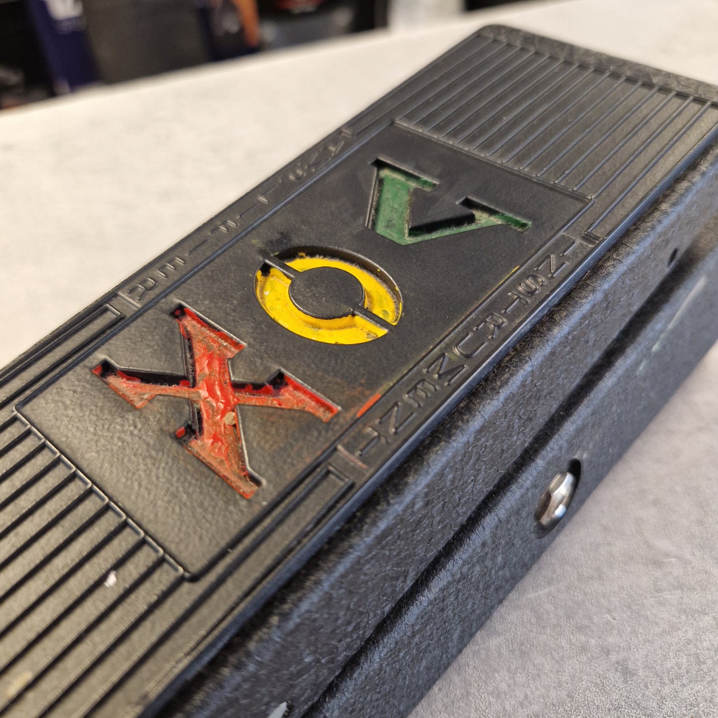 Pre-Owned Vox V845 Close-up of a black textured electronic device with the letters 'VOX' in green, yellow, and red on the front.