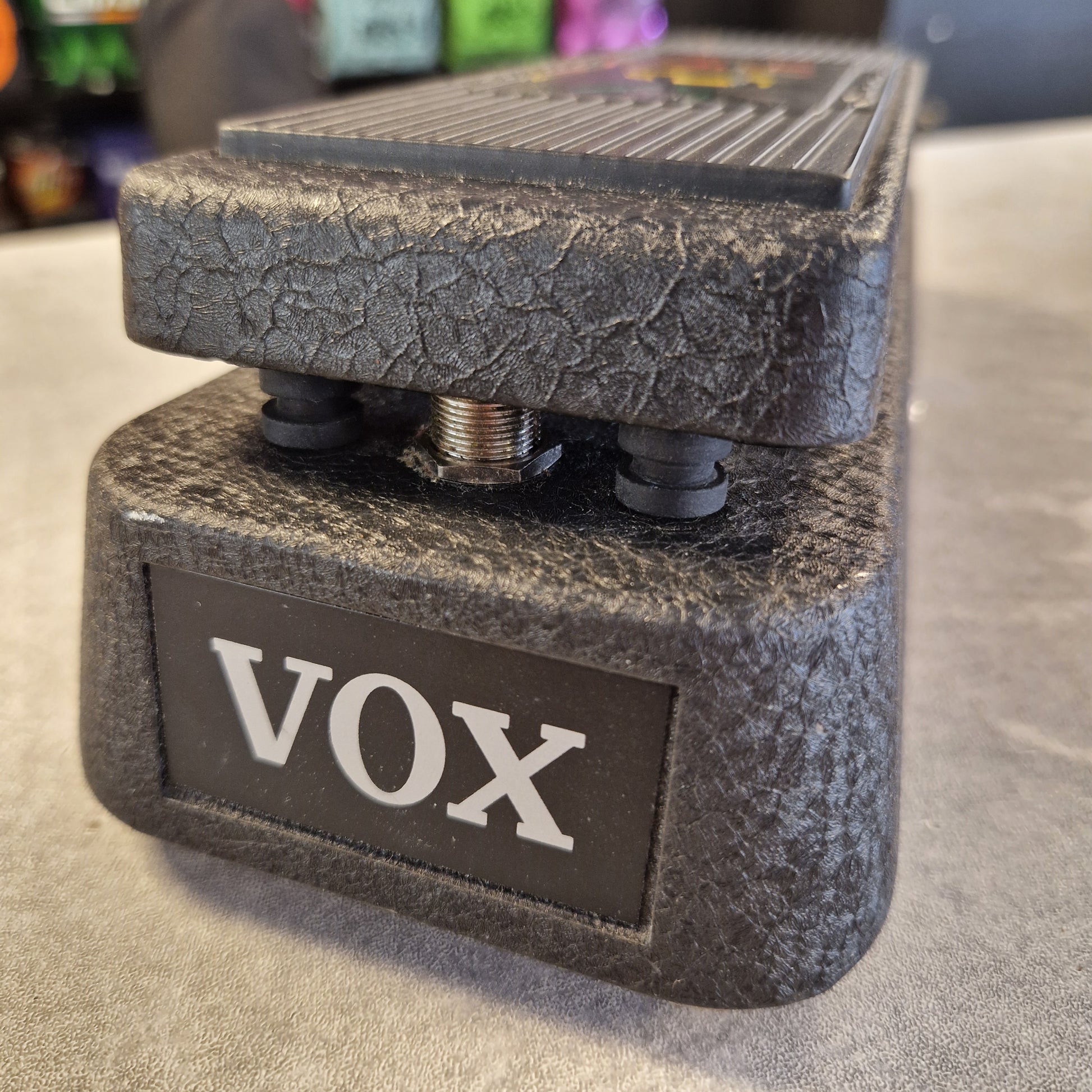 Pre-Owned Vox V845 A close-up of a Vox guitar effects pedal with a textured dark gray footplate and a black brand badge with white lettering, resting on a light gray surface.