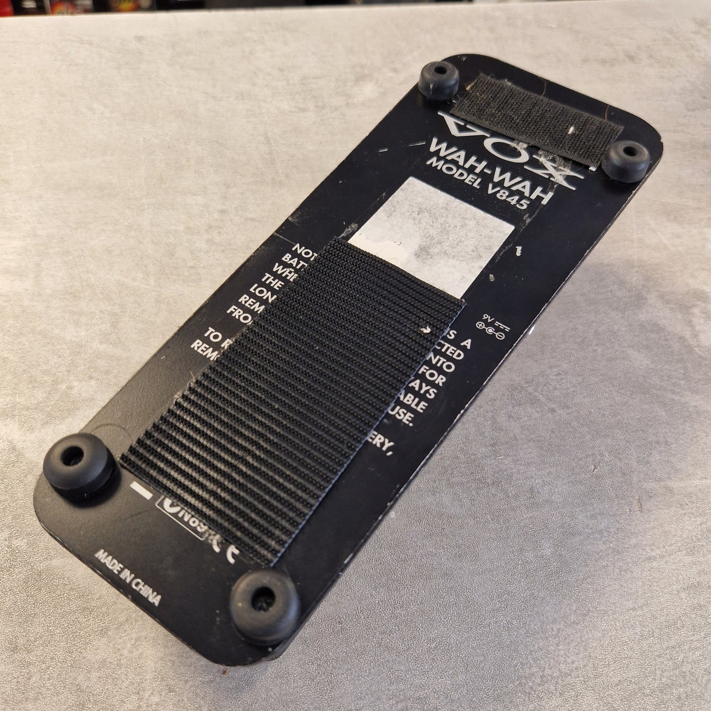 Pre-Owned Vox V845 A black Wahvat Model 1985 portable radio shown from the bottom, featuring a textured speaker grille, control knobs, and various white printed labels and markings, resting on a gray textured surface.