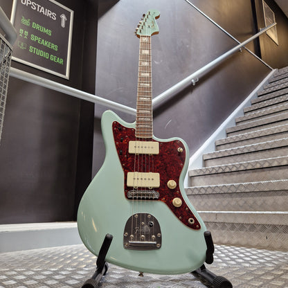 Pre-Owned Fender A mint green electric guitar with a red glitter pickguard and cream humbucker pickups, displayed on a stand in a studio setting.