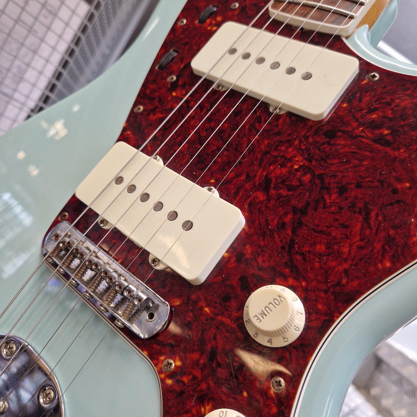Pre-Owned Fender Close-up of a guitar body showing a red tortoiseshell pickguard, cream humbucker pickups, chrome hardware, and a pale mint green edge.