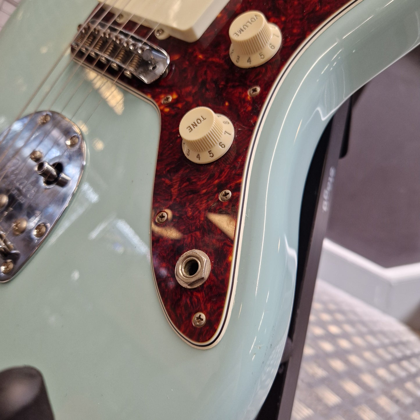 Pre-Owned Fender Close-up of an electric guitar body showing a pale mint green finish, a dark red tortoiseshell pickguard, cream control knobs, and part of the chrome bridge.