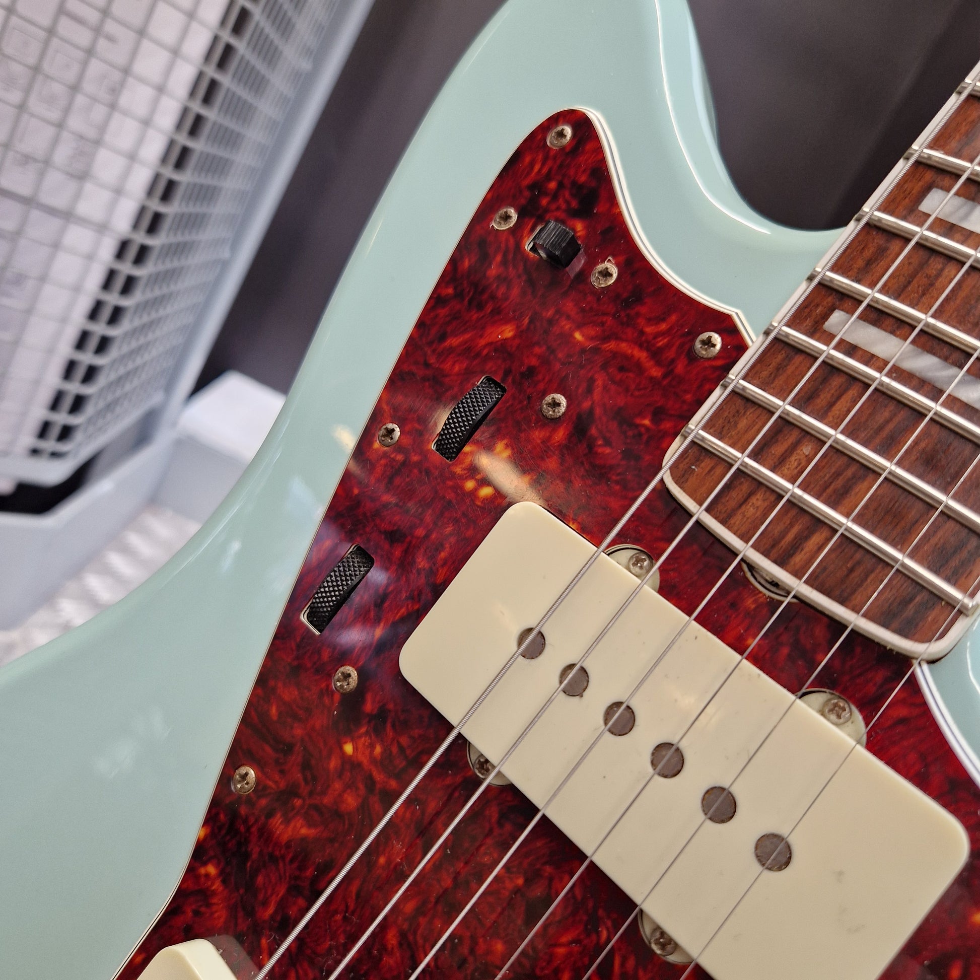 Pre-Owned Fender Close-up of an electric guitar showing a mint green body, a red and black tortoiseshell pickguard, cream humbucker pickups, and a dark wood fretboard.