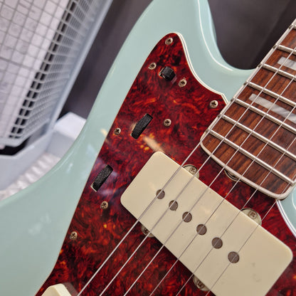 Pre-Owned Fender Close-up of an electric guitar showing a mint green body, a red and black tortoiseshell pickguard, cream humbucker pickups, and a dark wood fretboard.