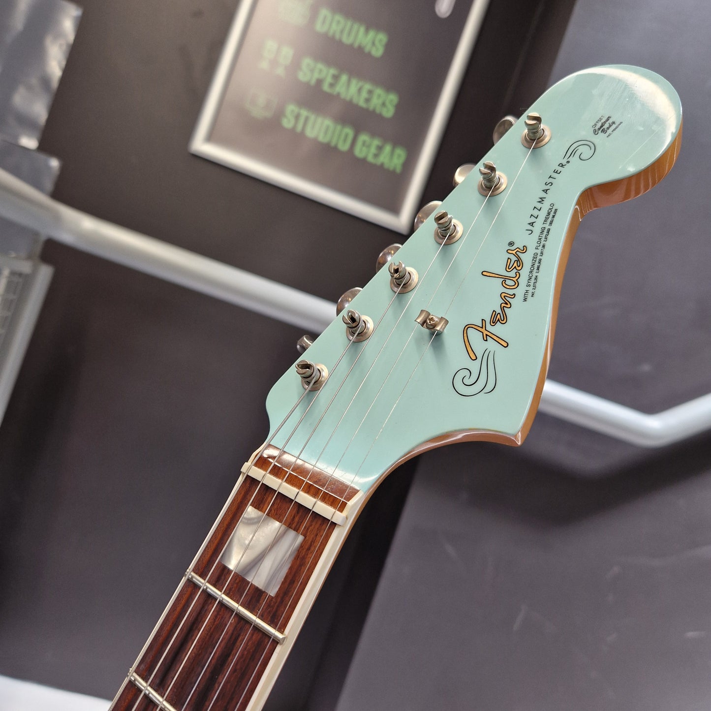 Pre-Owned Fender Close-up of a Fender Jazzmaster electric guitar headstock in mint green, showing the gold Fender logo, six silver tuning pegs, and part of the dark brown fretboard against a dark background.
