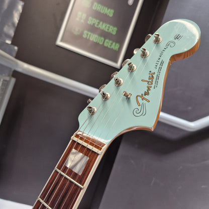 Pre-Owned Fender Close-up of a Fender Jazzmaster electric guitar headstock in mint green, showing the gold Fender logo, six silver tuning pegs, and part of the dark brown fretboard against a dark background.