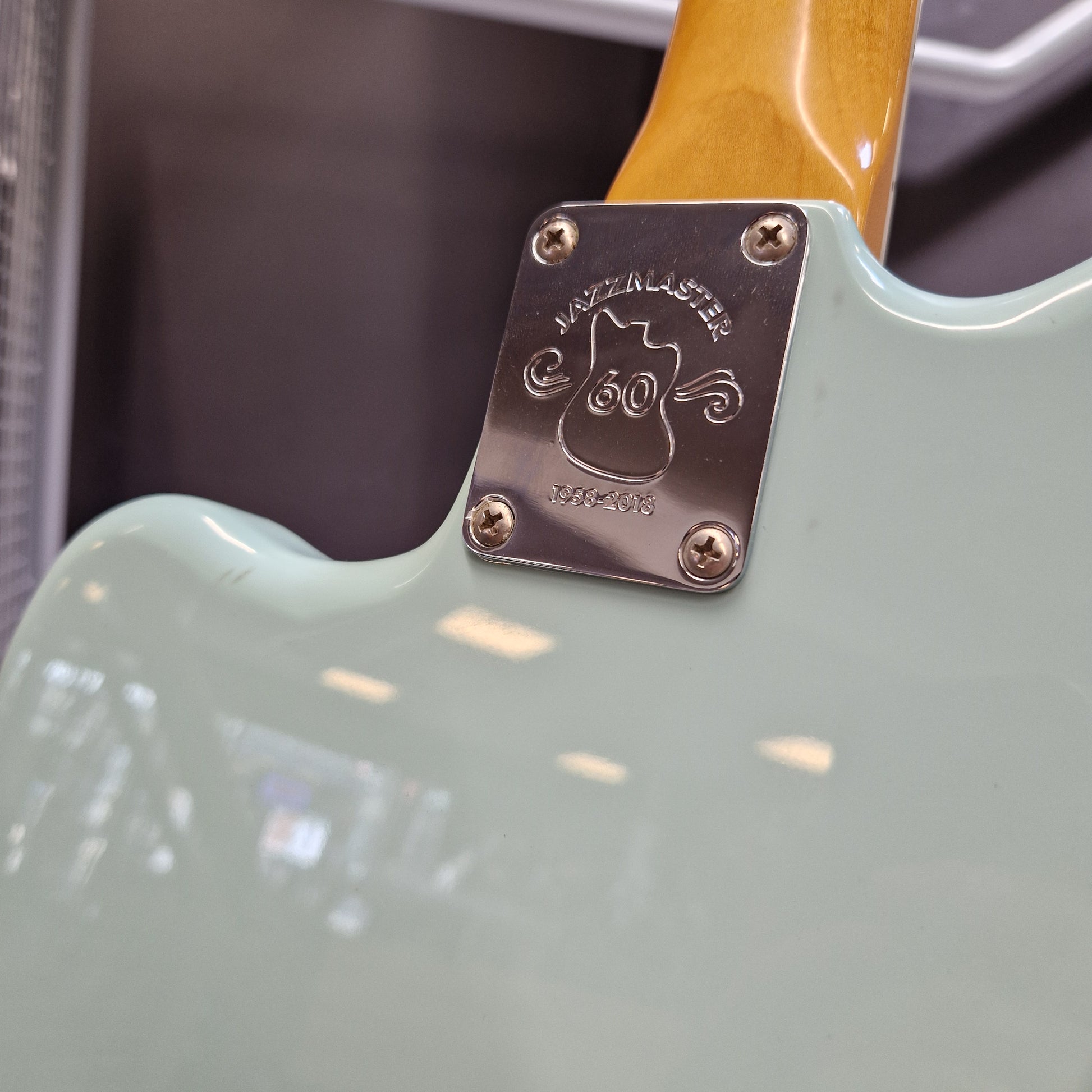 Pre-Owned Fender Close-up of the back of an electric guitar showing a mint green body, a maple wood neck, and a metal plate engraved with the Fender logo and 'FENDER' text.