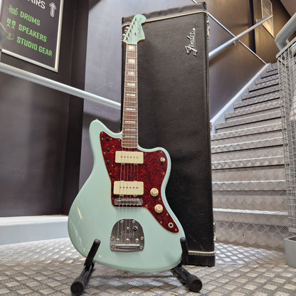Pre-Owned Fender A mint green Fender Stratocaster electric guitar with a red glitter pickguard, resting on a black Fender amp head against a textured metal wall.