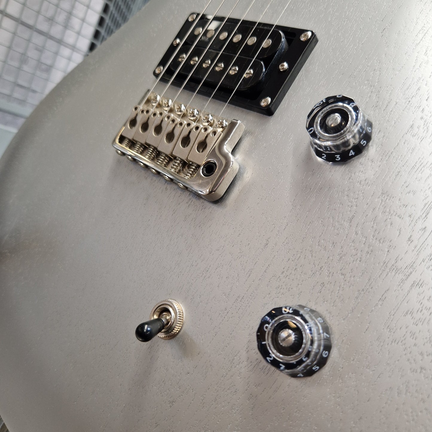 Pre-Owned PRS SE CE24 Close-up of the lower bout body of an electric guitar showing the silver body finish, black bridge, silver hardware, and a small black toggle switch.