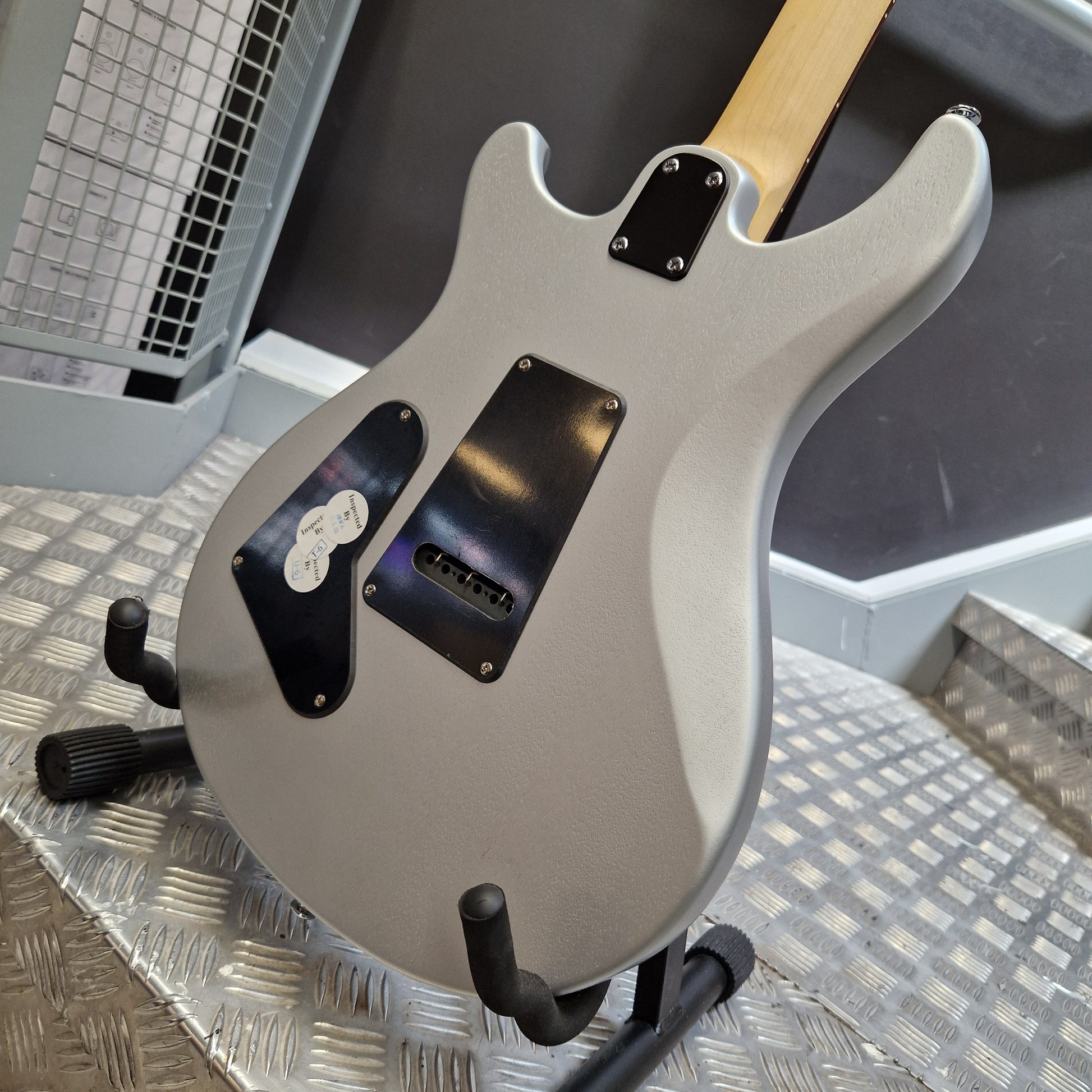 Pre-Owned PRS SE CE24 Silver electric guitar body with black pickguard and hardware, resting on a metal stand on a diamond plate floor.
