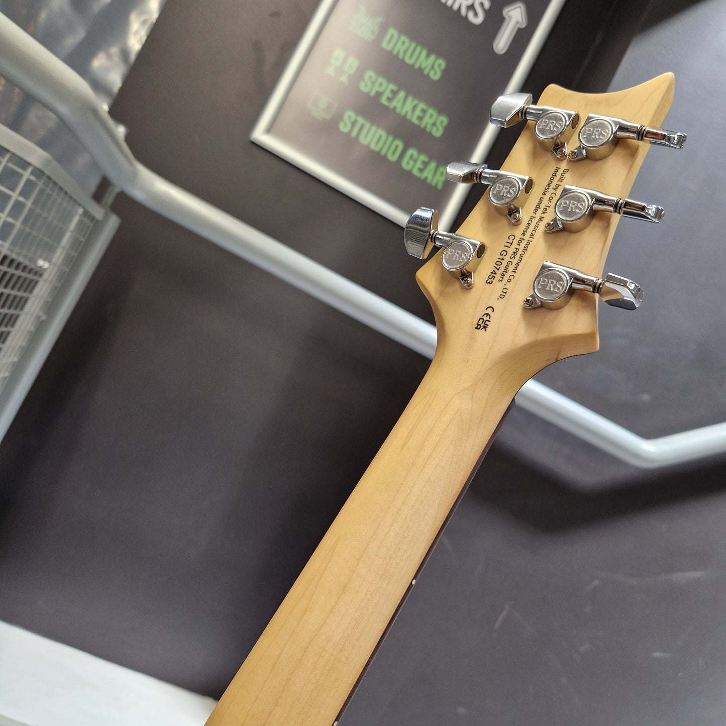 Pre-Owned PRS SE CE24 Close-up of a light natural wood drum headstock with six silver tuning pegs, photographed inside a storage or display case.