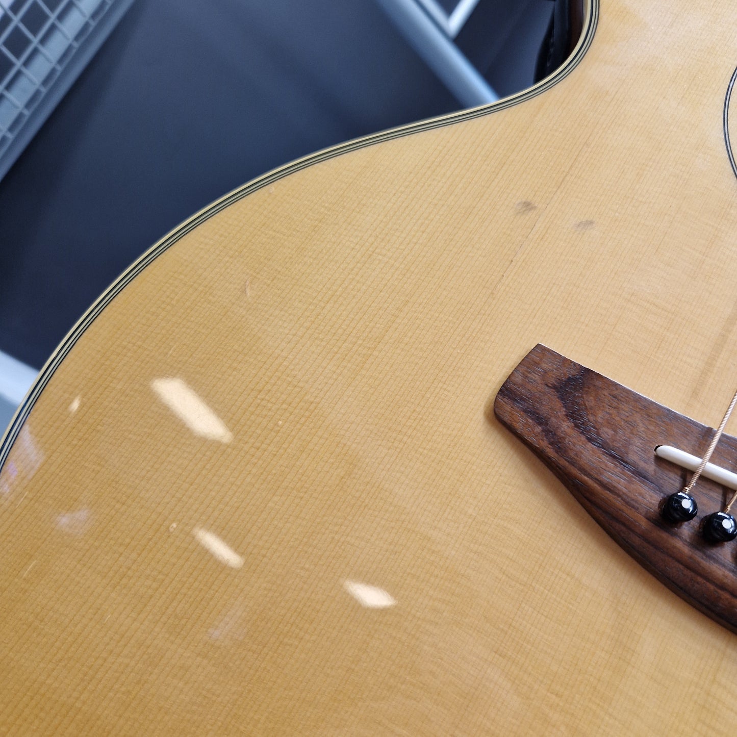 Pre-Owned Yamaha CPX700 Close-up of an acoustic guitar body showing the natural wood grain finish, the bridge, and part of the sound hole rim.