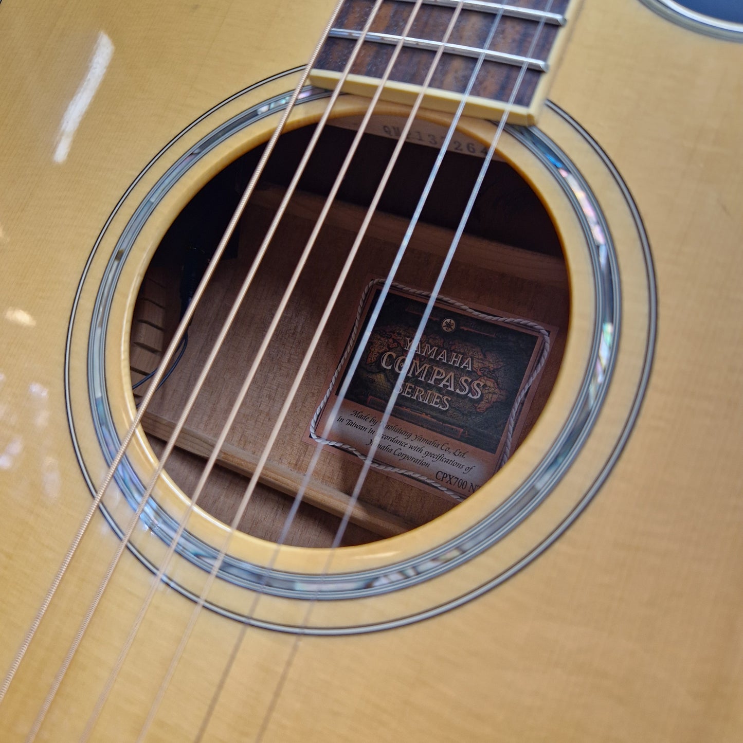 Pre-Owned Yamaha CPX700 Close-up of an acoustic guitar's soundhole and part of the neck, showing the Yamaha logo and 'Compass Series' label inside the hole.