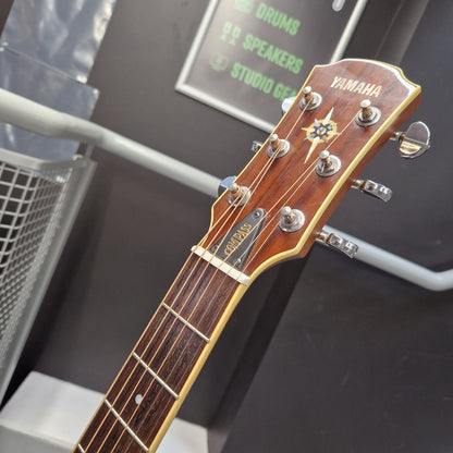 Pre-Owned Yamaha CPX700 Close-up of a Yamaha guitar headstock and neck, showing the Yamaha logo, tuning pegs, and fretboard against a dark indoor background.