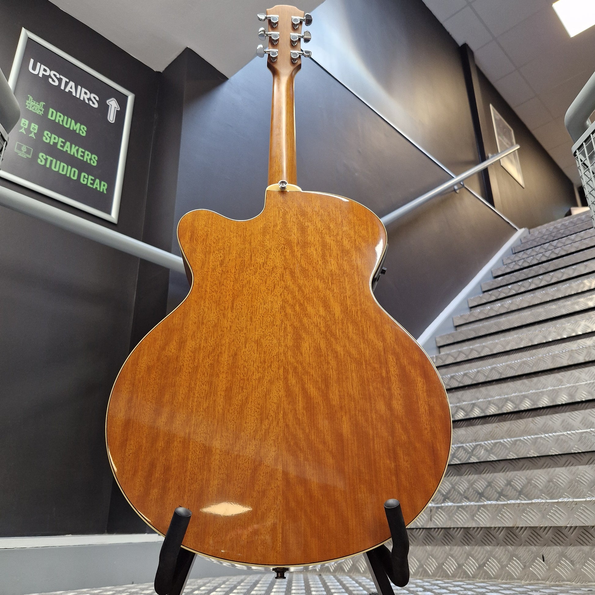 Pre-Owned Yamaha CPX700 A glossy brown acoustic guitar body shown from the back, mounted on a display stand in a showroom or studio setting.