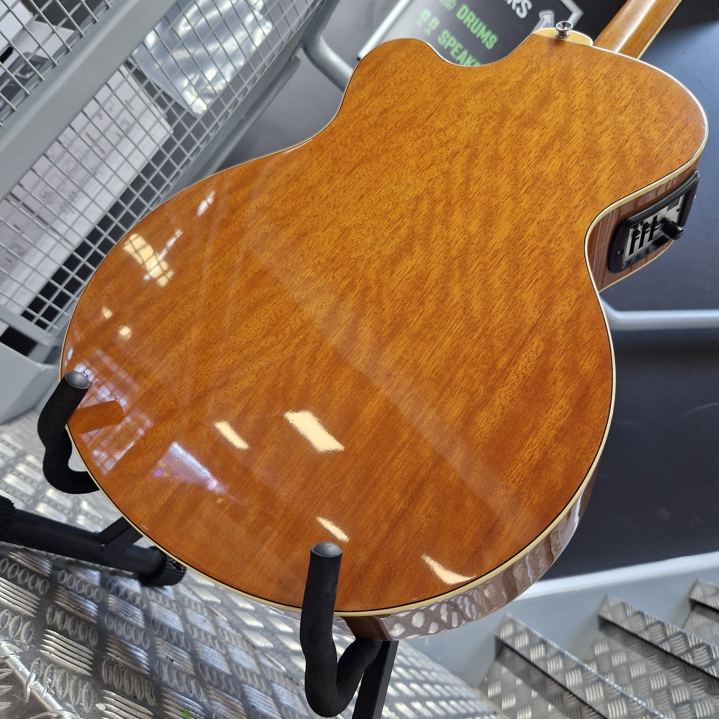 Pre-Owned Yamaha CPX700 Close-up of the glossy back of an electric guitar showing a warm honeyburst wood finish, resting on a black stand.