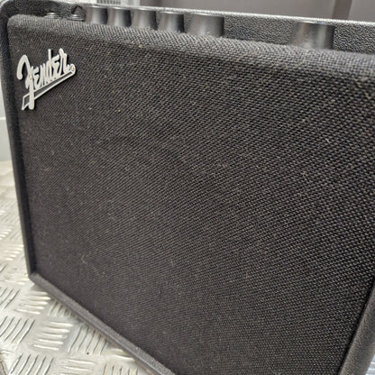 Pre-Owned Fender Close-up of a black Fender speaker grille with the silver Fender logo in the lower-left corner, set against a silver diamond plate background.