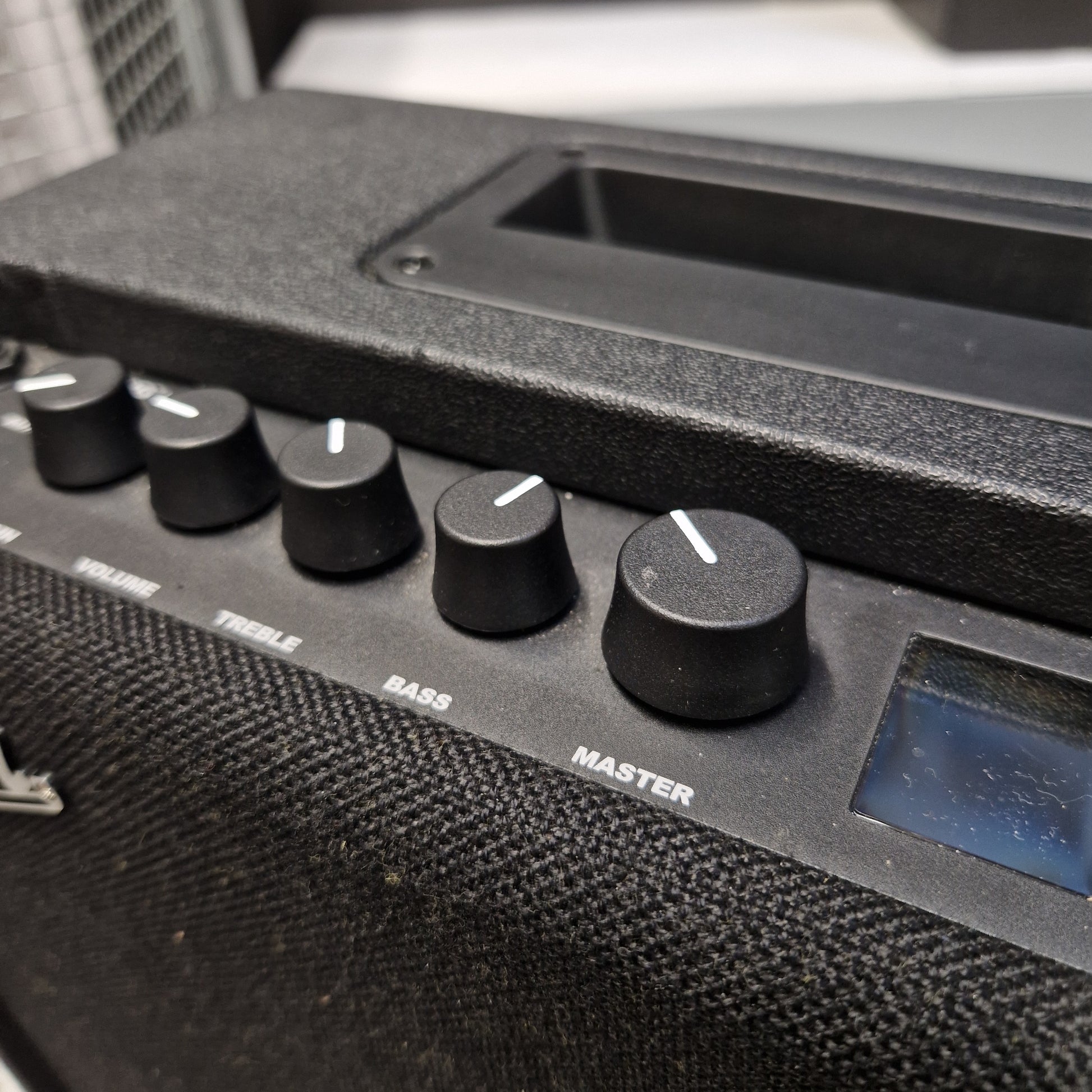 Pre-Owned Fender Close-up of a black electronic speaker or amplifier control panel with multiple rotary knobs and a small display screen.