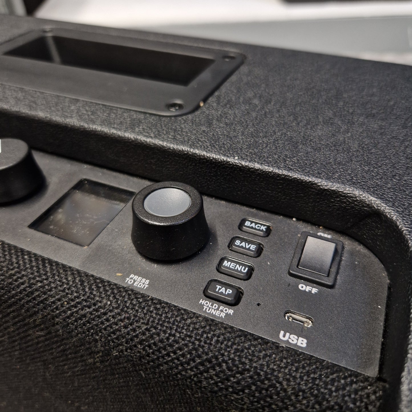 Pre-Owned Fender Close-up of a black electronic control panel with buttons, a rotary knob, a small display, and a textured speaker grille.