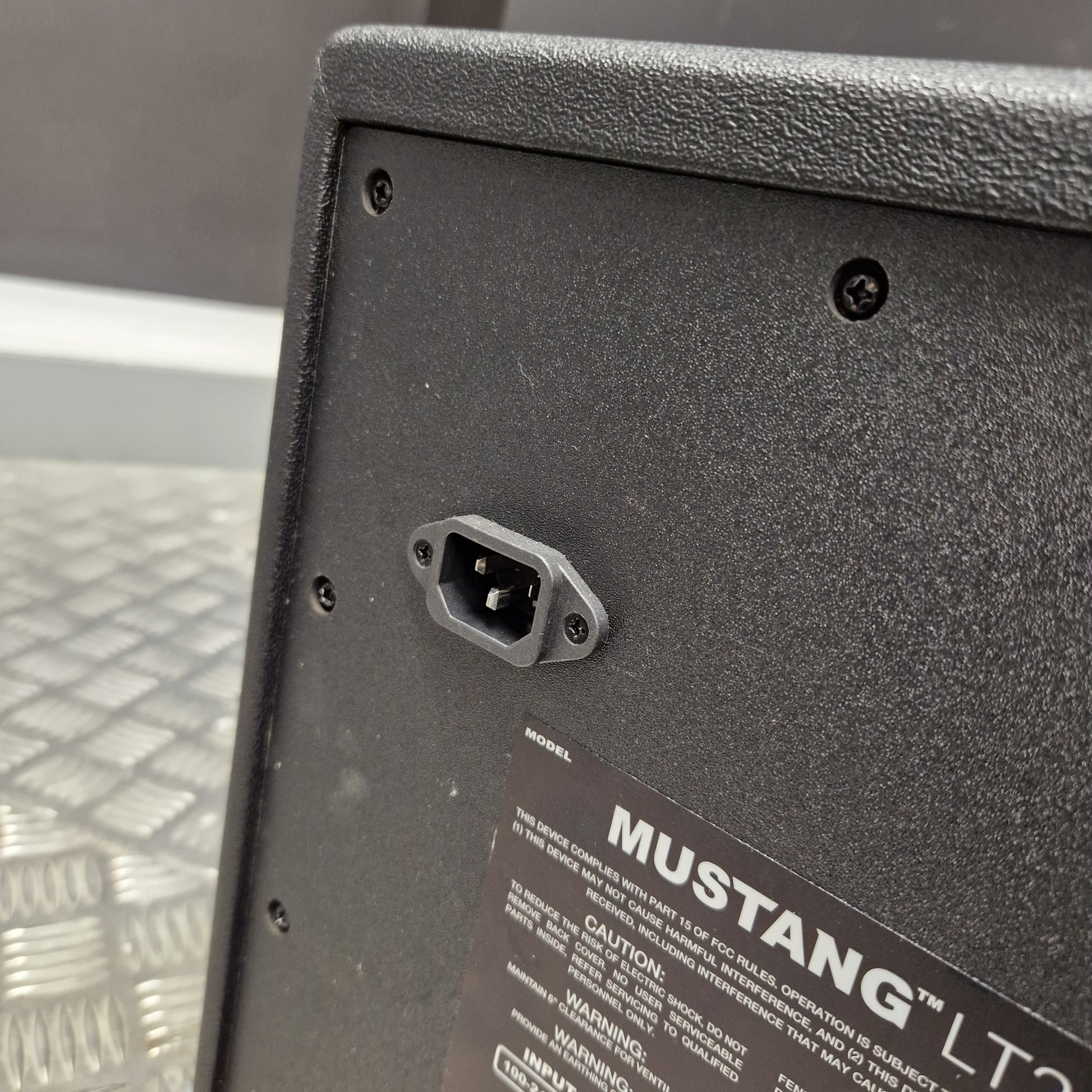 Pre-Owned Fender Close-up of the rear lower corner of a black Mustang LT200 amplifier, showing a power input socket and part of the product label.