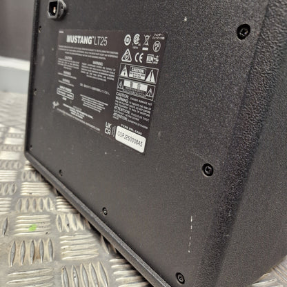 Pre-Owned Fender Close-up of the underside of a black metal equipment housing or panel, showing screws, a product label, and a power cord connector, resting on a silver diamond plate.
