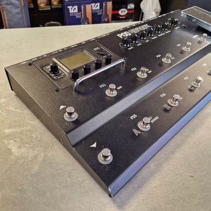 Pre-Owned Line 6 A black multi-effects guitar pedal with silver footswitches and knobs, photographed at an angle on a gray concrete floor with a store shelf visible in the background.