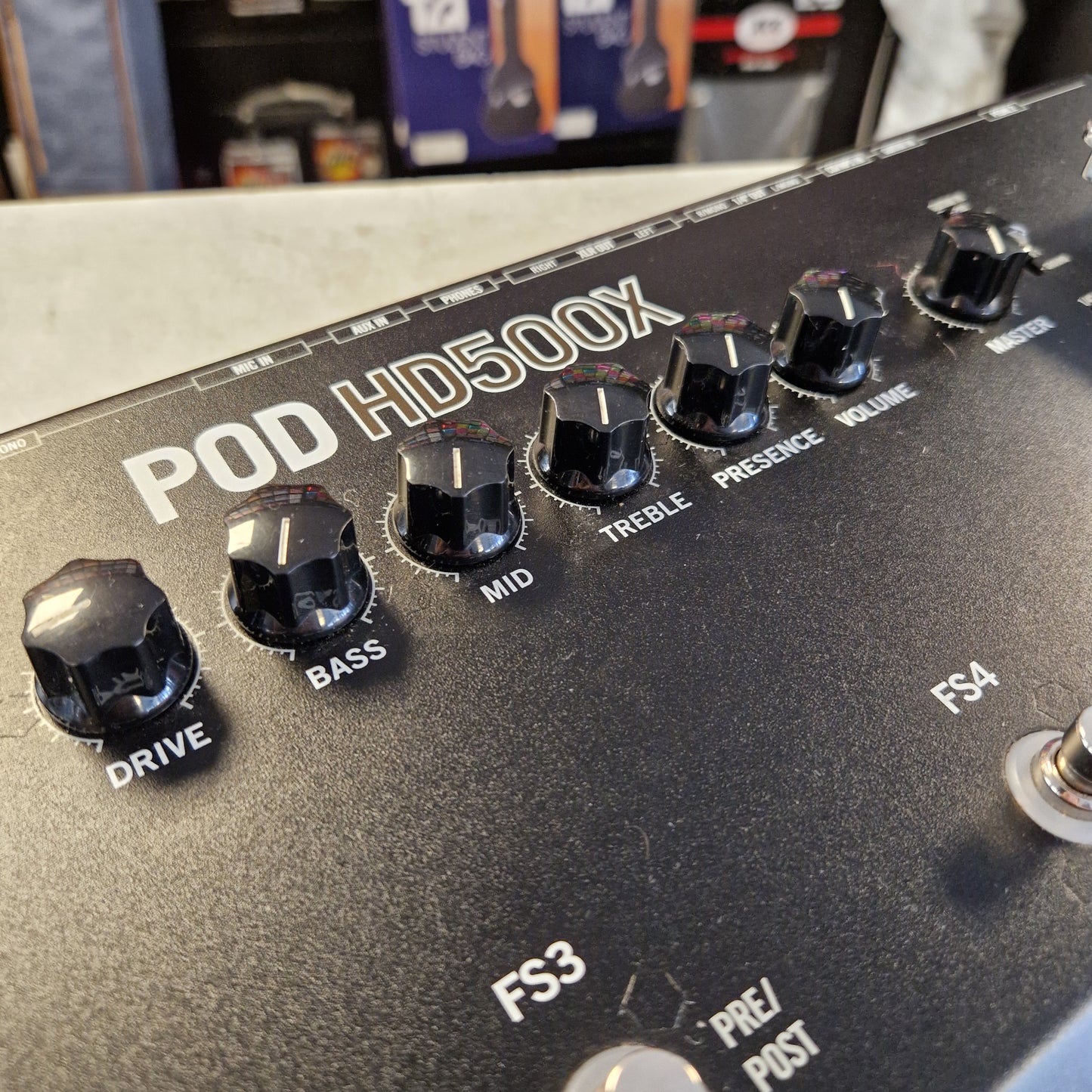Pre-Owned Line 6 Close-up of a black guitar effects pedal control panel labeled POD HD500X, showing multiple black rotary knobs with white labels including BASS, DRIVE, MID, TREBLE, PRECESSION, and WAVE.