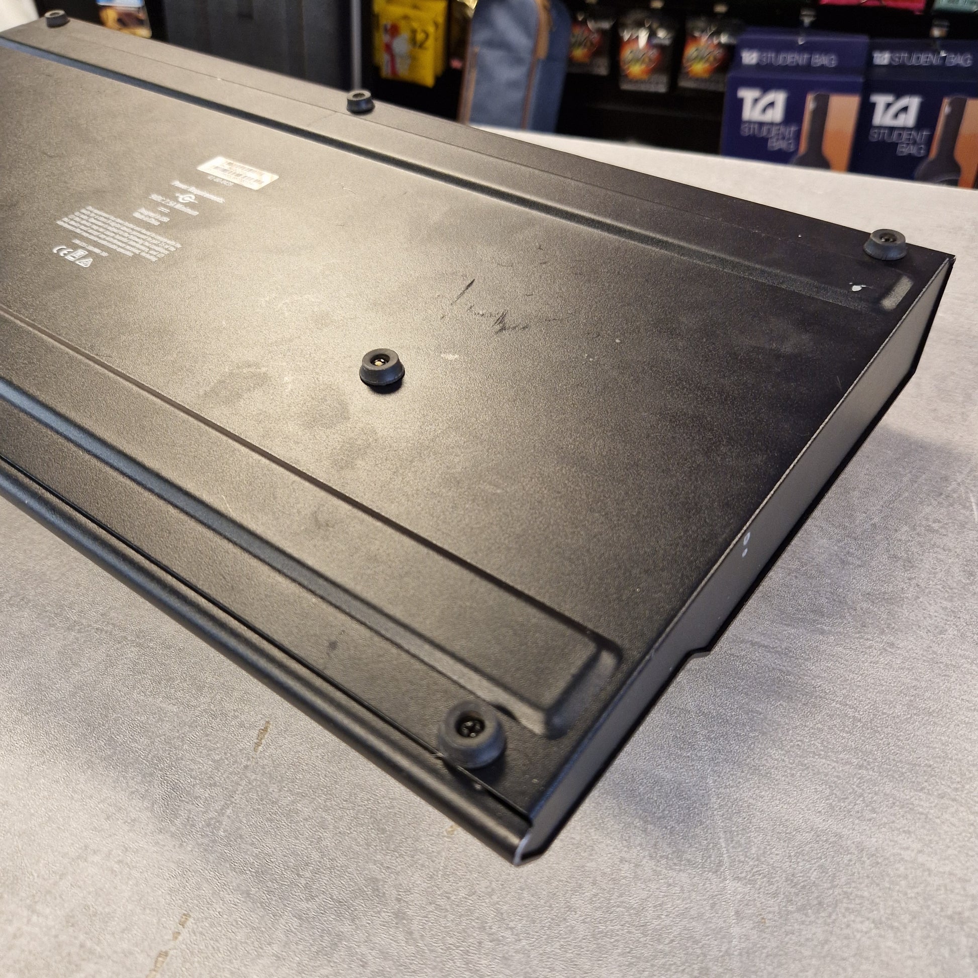 Pre-Owned Line 6 A black metal electronic component or enclosure panel with screws and printed technical labels, photographed on a gray floor with store shelves visible in the background.