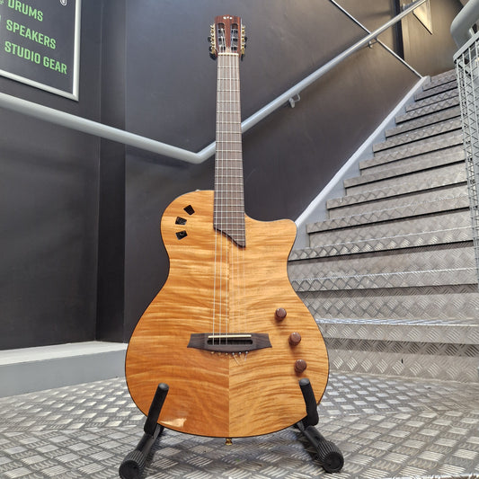 Pre-Owned Cordoba Stage A natural wood cutaway acoustic-electric guitar displayed on a stand in an indoor showroom or studio space with metal grating walls and a staircase.