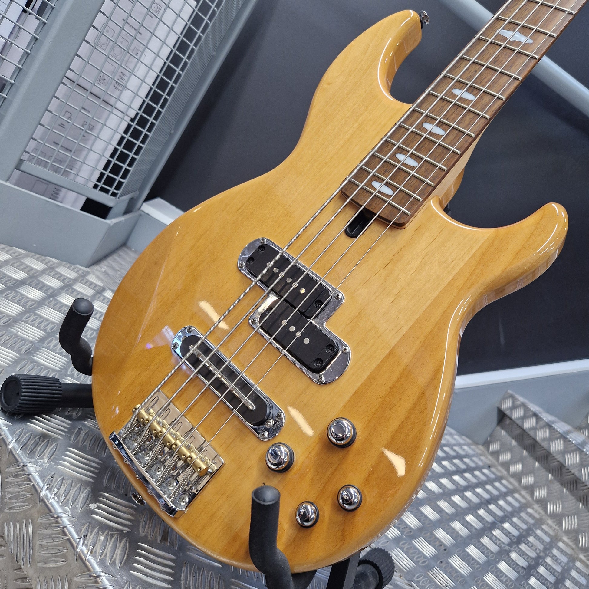 Pre-Owned Yamaha BB615 A natural wood five-string bass guitar with chrome hardware, shown resting on a metal stand in a workshop setting.