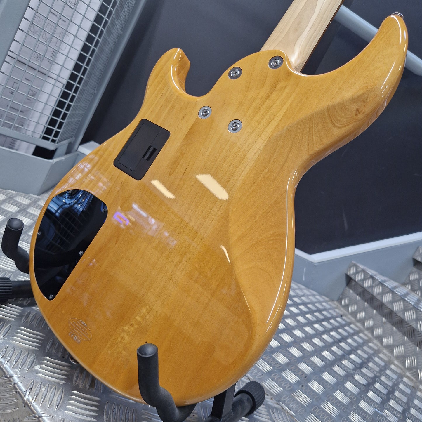 Pre-Owned Yamaha BB615 Close-up of the back of a glossy natural wood electric guitar body on a metal stand, with a dark gray background.