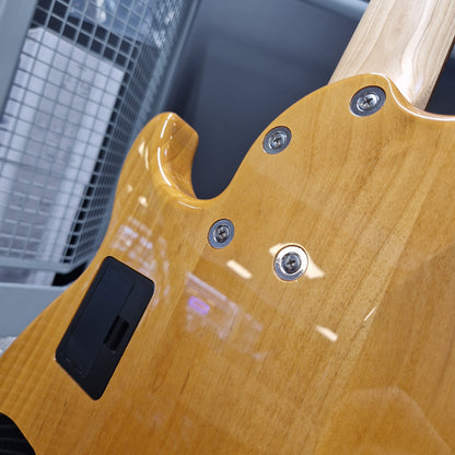 Pre-Owned Yamaha BB615 Close-up of the back of a glossy natural wood electric guitar body with visible control screws and a black pickup cover, photographed indoors against a gray industrial background.