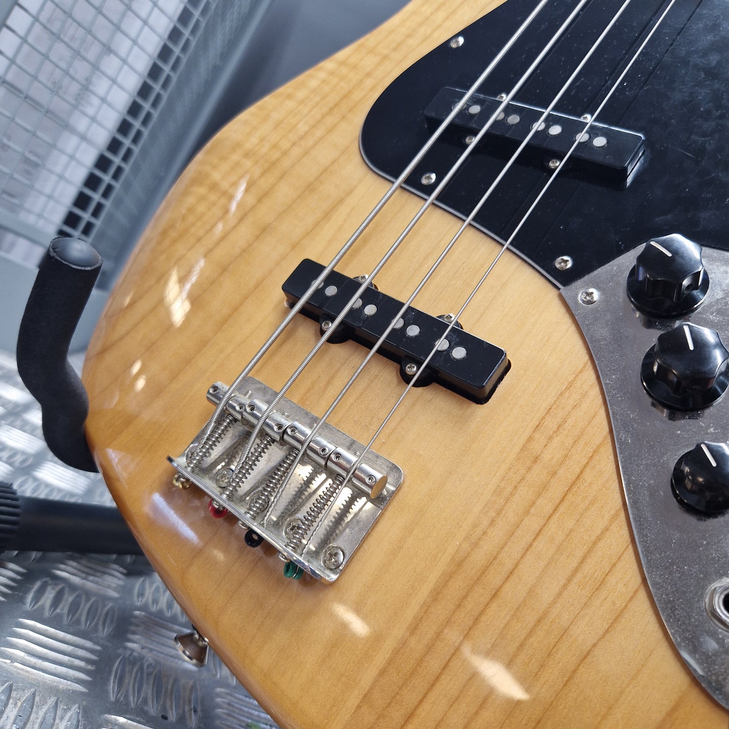 Pre-Owned Squier  Close-up of a natural wood four-string bass guitar showing the body, black pickguard, pickups, bridge, and part of the control knobs.