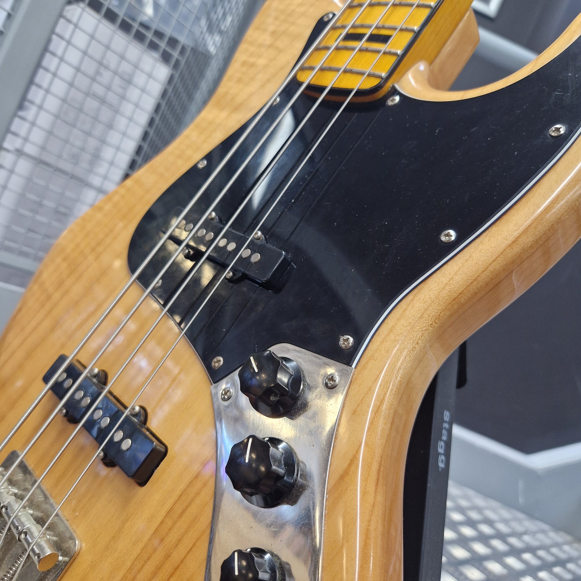 Pre-Owned Squier  Close-up of a bass guitar body showing the natural wood finish, black pickguard, chrome hardware, and four control knobs.