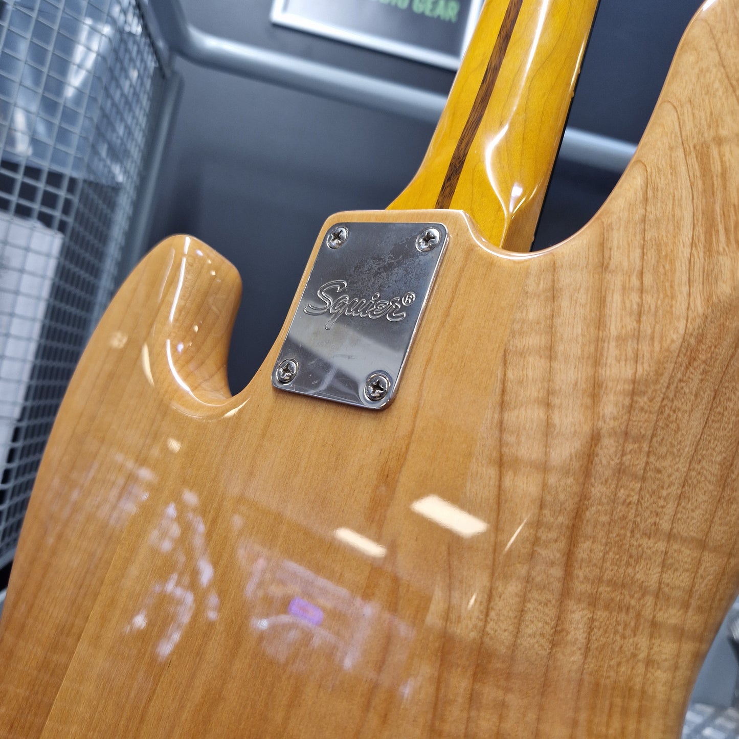 Pre-Owned Squier  Close-up of the back of a guitar body with a glossy natural wood finish and a silver metal plate secured by four screws.