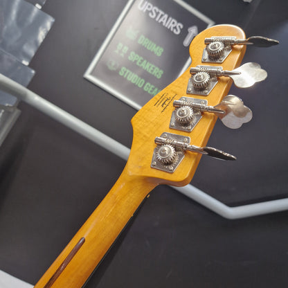 Pre-Owned Squier  Close-up of a four-string bass guitar headstock with a natural maple wood finish and silver tuning pegs, photographed indoors against a dark gray background.