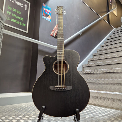 Pre-Owned Tanglewood TWBBSFCELH A black acoustic-electric guitar with a cutaway body and six strings, photographed indoors against a dark wall with metal paneling and stairs in the background.