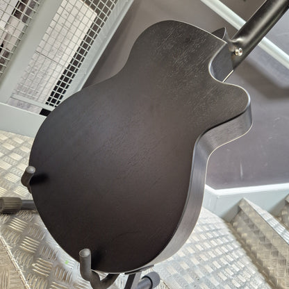 Pre-Owned Tanglewood TWBBSFCELH Close-up of the back of a dark wood acoustic guitar body on a stand, showing the natural wood grain and hardware against a metal grid background.