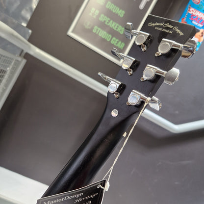 Pre-Owned Tanglewood TWBBSFCELH Close-up of a black guitar headstock with silver tuning pegs and a tag reading 'MasterTone Studio Gear' attached, photographed indoors against a dark surface.