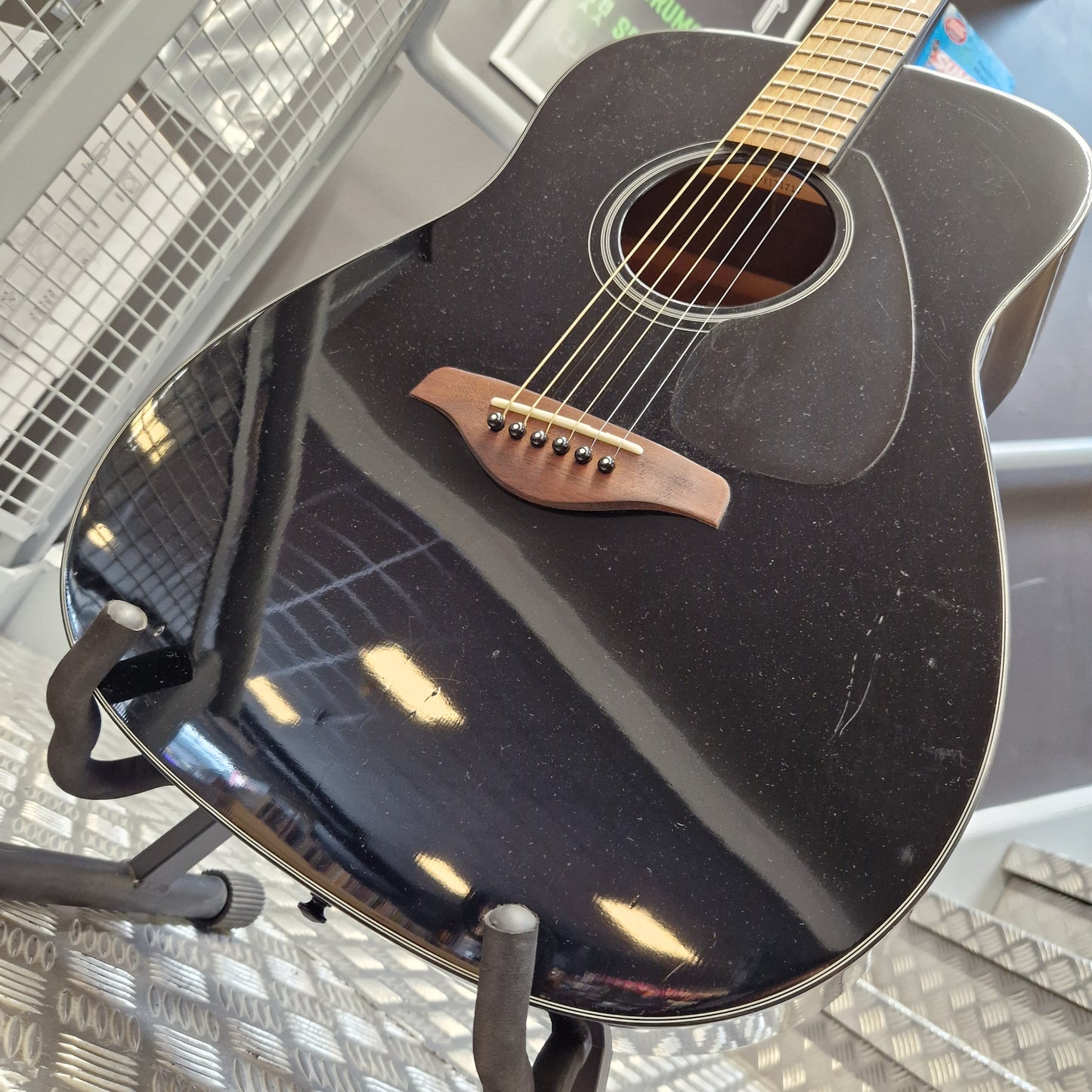 Pre-Owned Yamaha FG800 Close-up of the side of a black acoustic guitar resting on a stand, showing the glossy finish, sound hole, bridge, and part of the neck.
