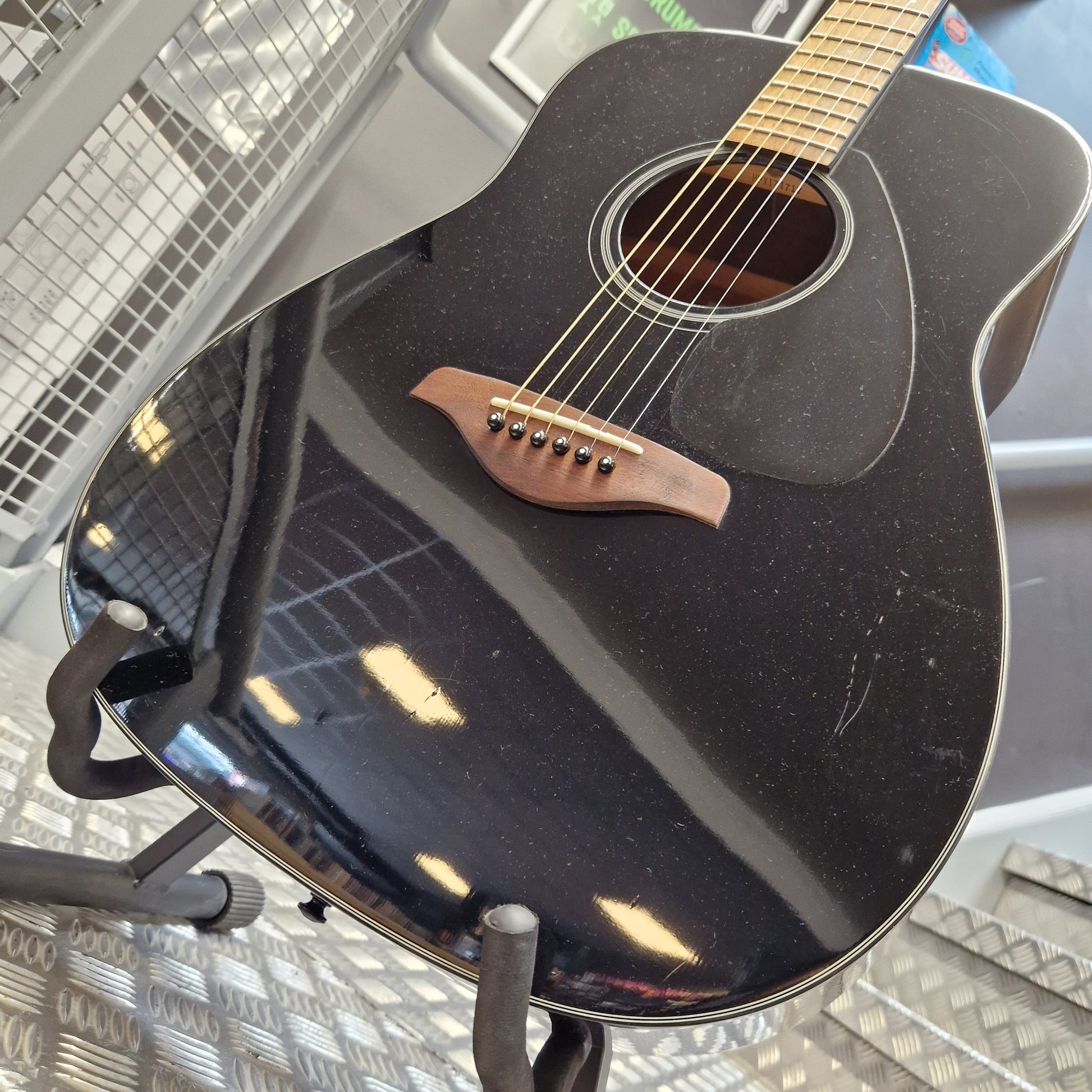 Pre-Owned Yamaha FG800 Close-up of the side of a black acoustic guitar resting on a stand, showing the glossy finish, sound hole, bridge, and part of the neck.