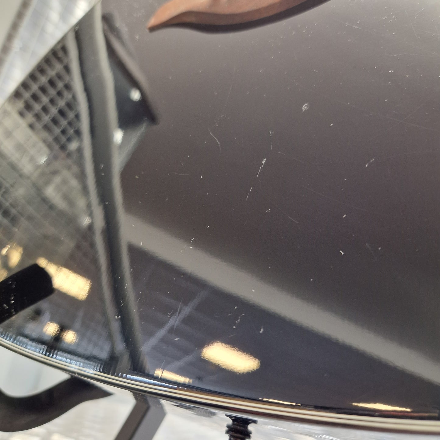 Pre-Owned Yamaha FG800 Close-up of a dark glossy surface with visible scratches and dust, likely part of a vehicle or appliance panel, with a small portion of a person's ear visible on the left edge.
