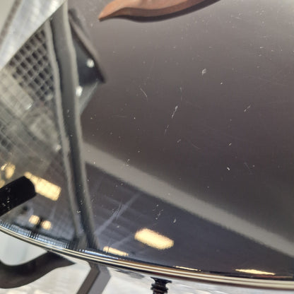 Pre-Owned Yamaha FG800 Close-up of a dark glossy surface with visible scratches and dust, likely part of a vehicle or appliance panel, with a small portion of a person's ear visible on the left edge.