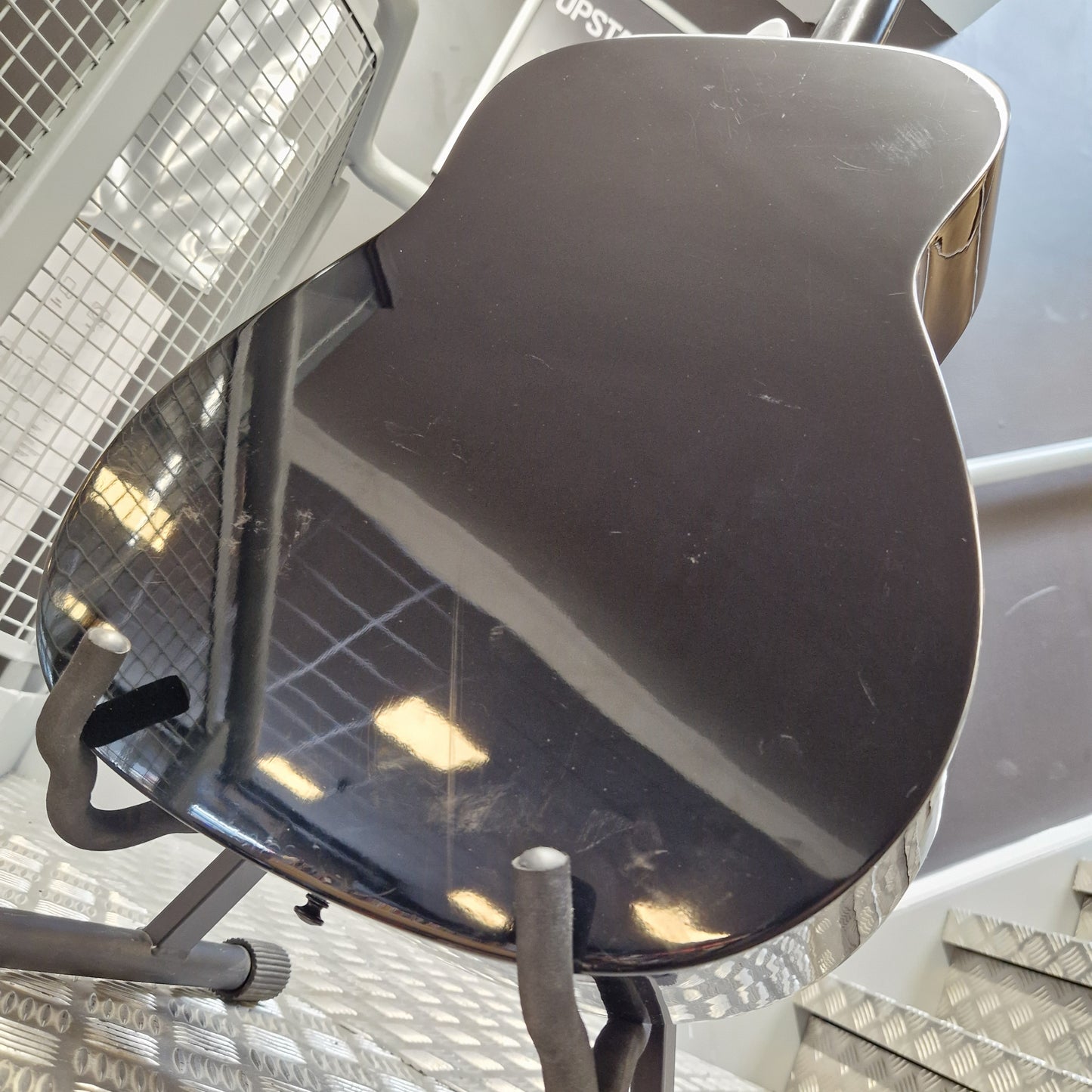 Pre-Owned Yamaha FG800 A close-up of a glossy black guitar body shell or decorative panel mounted on a metal rack, with reflections of the surrounding shop environment visible on the surface.