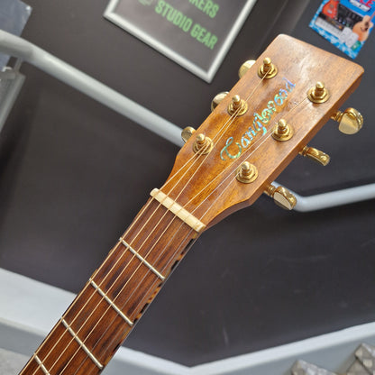 Pre-Owned Tanglewood TW15ASMNAT Close-up of a wooden acoustic guitar headstock with gold tuning pegs and strings, showing the brand name 'Crown' in green script on a dark display background.