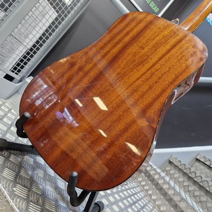 Pre-Owned Tanglewood TW15ASMNAT Close-up of the glossy back of an acoustic guitar showing rich wood grain, resting on a stand in a workshop setting.